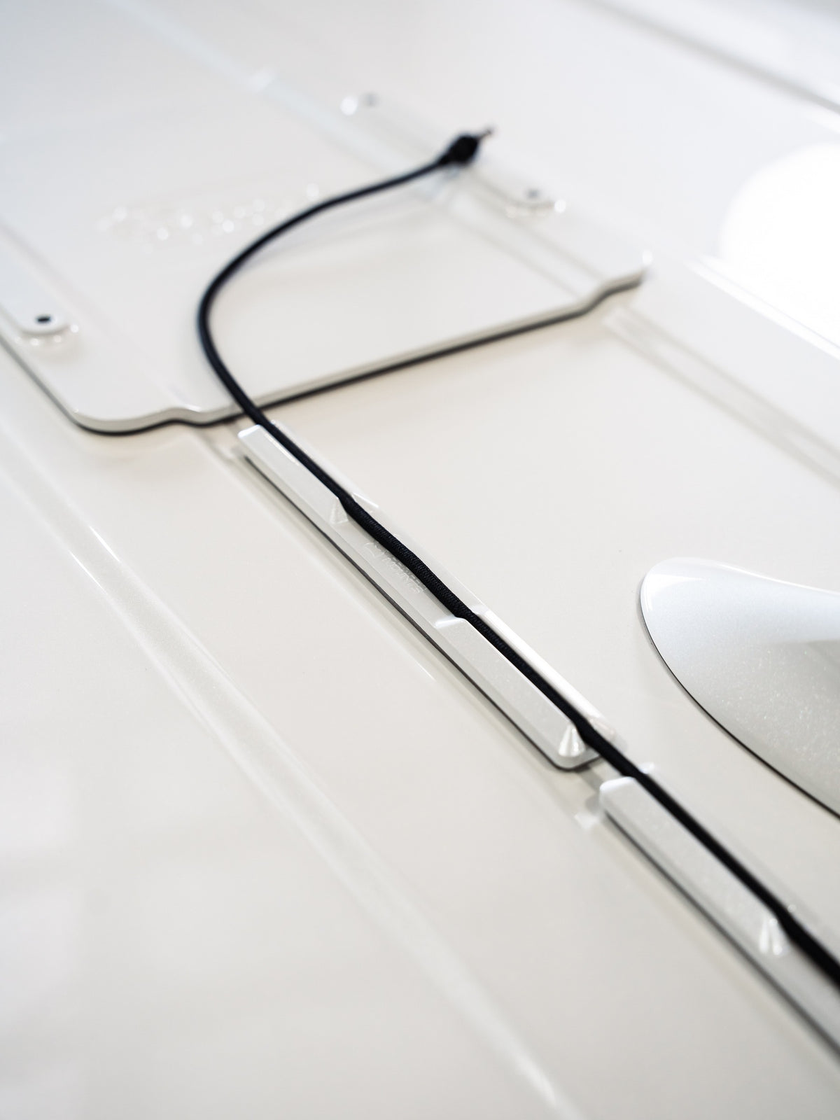 White VHB cable runners routing a black cable towards a Gorilla Mounts roof plate. Mounting plate and cable shown for installation context.