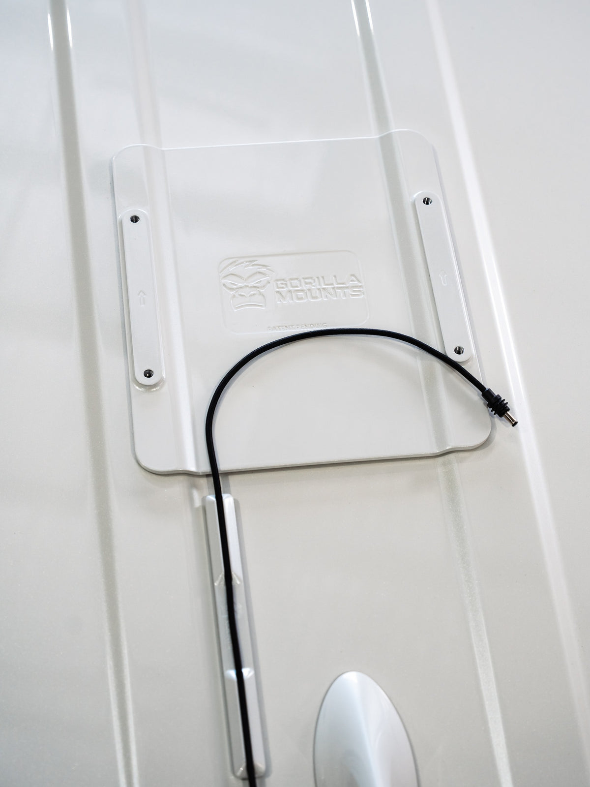 Top view of a white VHB cable runner guiding a black cable from a Gorilla Mounts roof plate. Mounting plate and cable are shown for context.